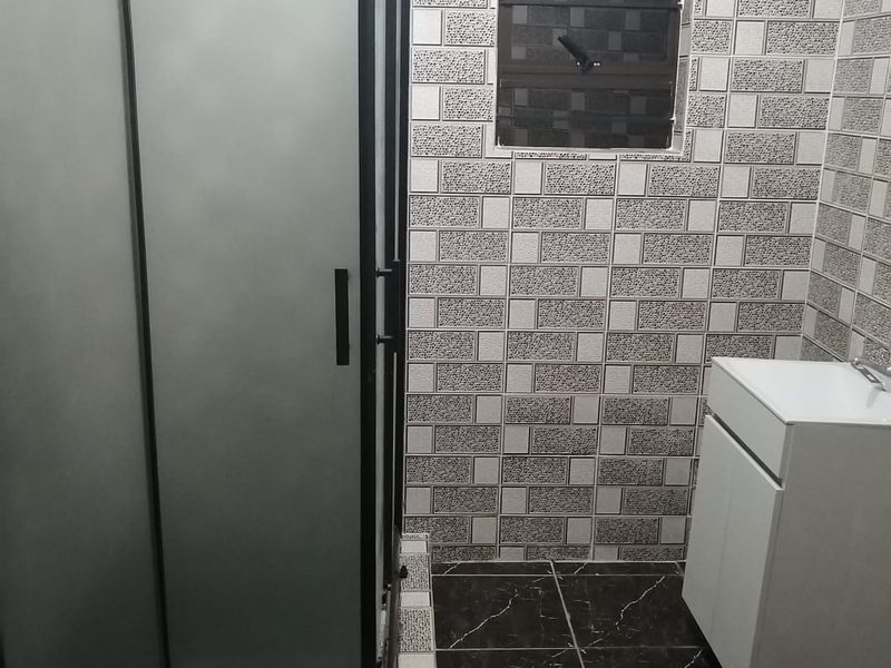 A modern bathroom featuring a glass shower enclosure, a white vanity cabinet with a basin, and contrasting tiled walls and flooring.