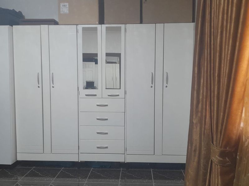 A bedroom featuring a large white built-in wardrobe with integrated drawers and mirror panels, complemented by dark tiled flooring.