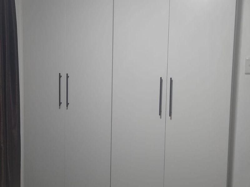 A bedroom featuring a modern, full-height built-in wardrobe with clean white cabinetry and minimalist handles.