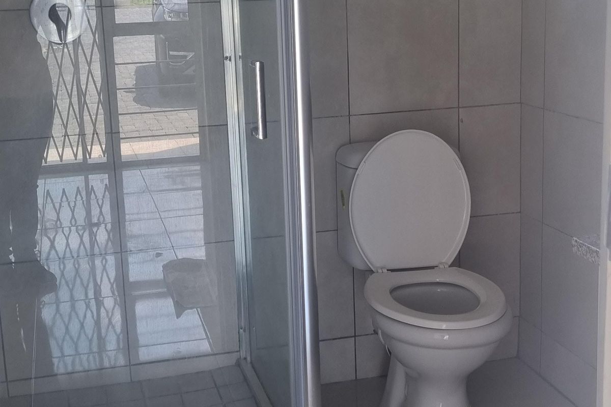 A functional bathroom featuring a glass-enclosed shower, a standard toilet, and neutral floor-to-ceiling tiling.