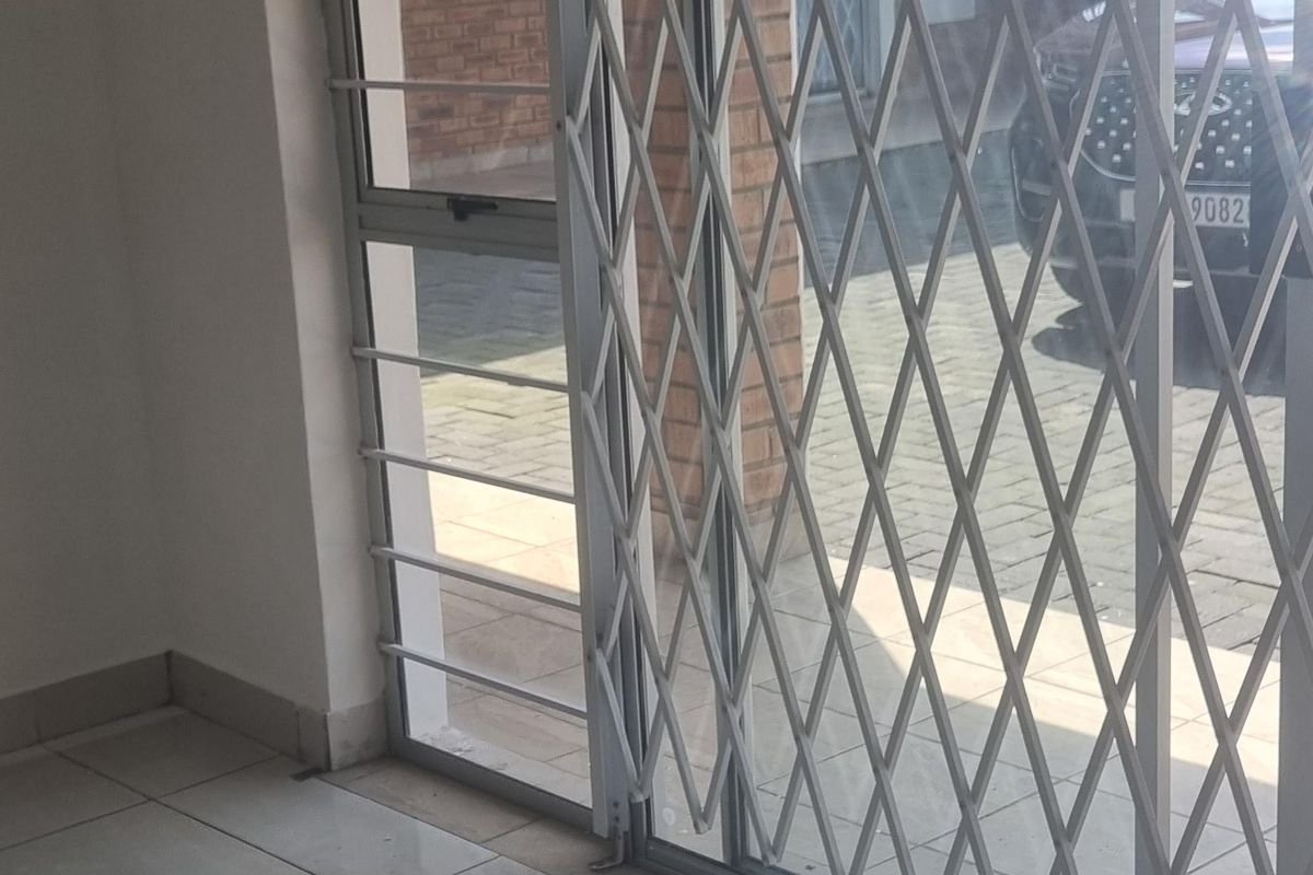 An empty living area featuring neutral ceramic floor tiles, a sliding glass door, and a fitted expandable security gate for added safety.