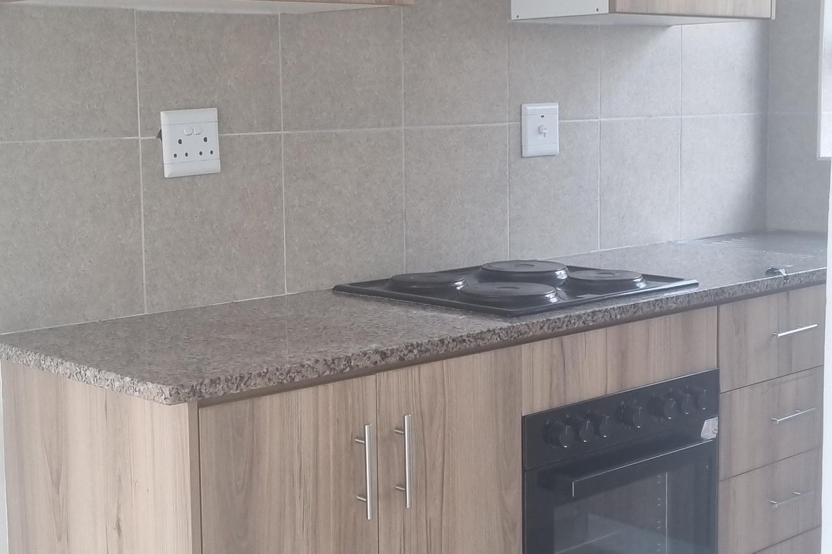 A clean, modern kitchen featuring light wood-finish cabinetry, granite countertops, a built-in oven, and an electric hob with a tiled backsplash.