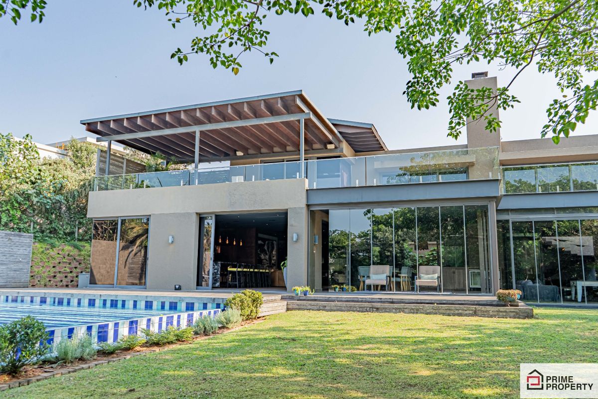A modern multi-level residence featuring a swimming pool, expansive glass sliding doors, a covered upper balcony, and a built-in outdoor fireplace.