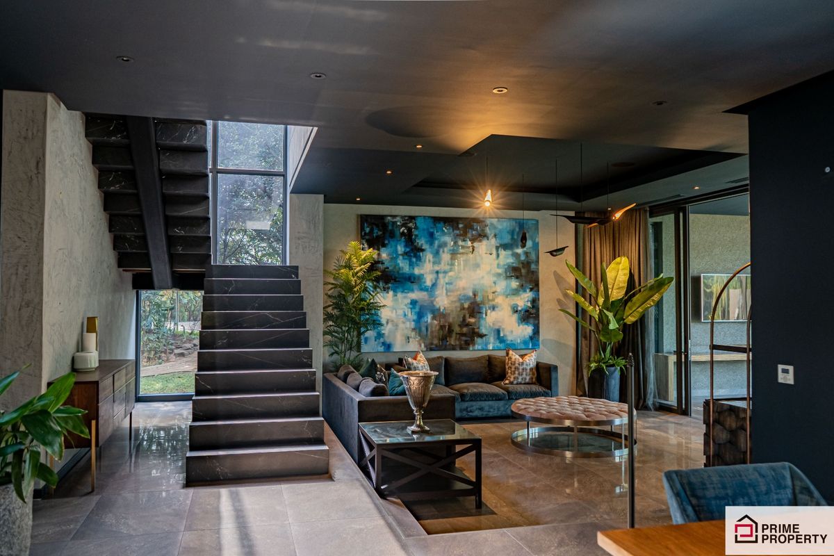 A sophisticated open-plan living area featuring a striking dark stone staircase, polished tile flooring, recessed ceiling lighting, and large windows overlooking the garden.