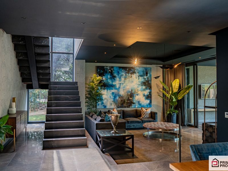A sophisticated open-plan living area featuring a striking dark stone staircase, polished tile flooring, recessed ceiling lighting, and large windows overlooking the garden.