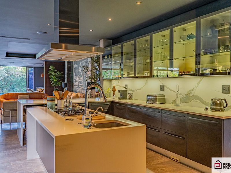 Modern open-plan kitchen featuring a central island, stone countertops, integrated cabinetry, glass-front display cupboards, and a stainless steel extractor hood.