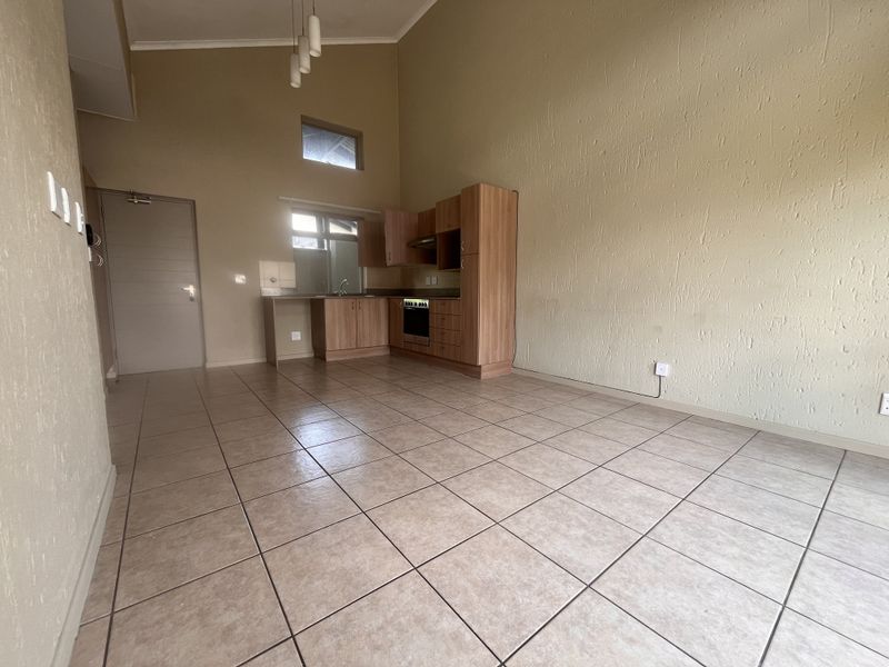 Spacious open-plan living area featuring tiled flooring, vaulted ceilings, and a functional kitchen with built-in cabinetry, oven, and extractor fan.