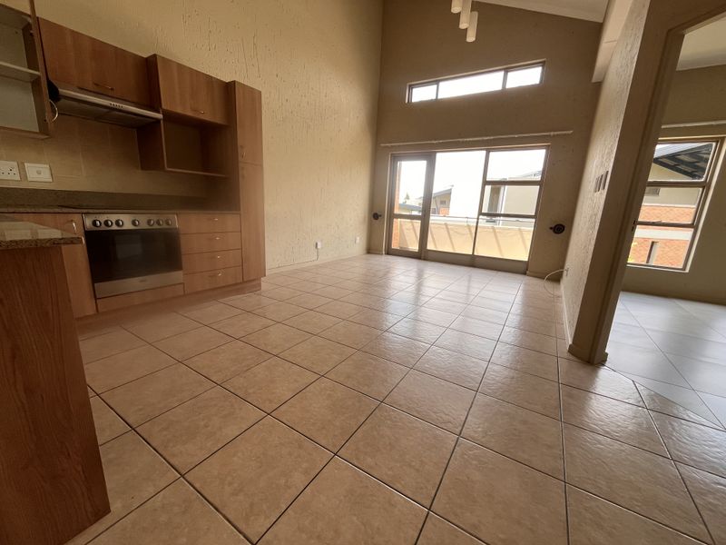 Spacious open-plan living and kitchen area featuring high vaulted ceilings, tiled flooring, and direct access to a balcony through sliding glass doors.