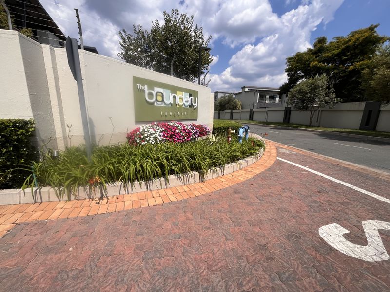 The entrance to The Boundary complex in Lonehill, featuring a paved driveway, landscaped garden, and secure boundary wall with electric fencing.