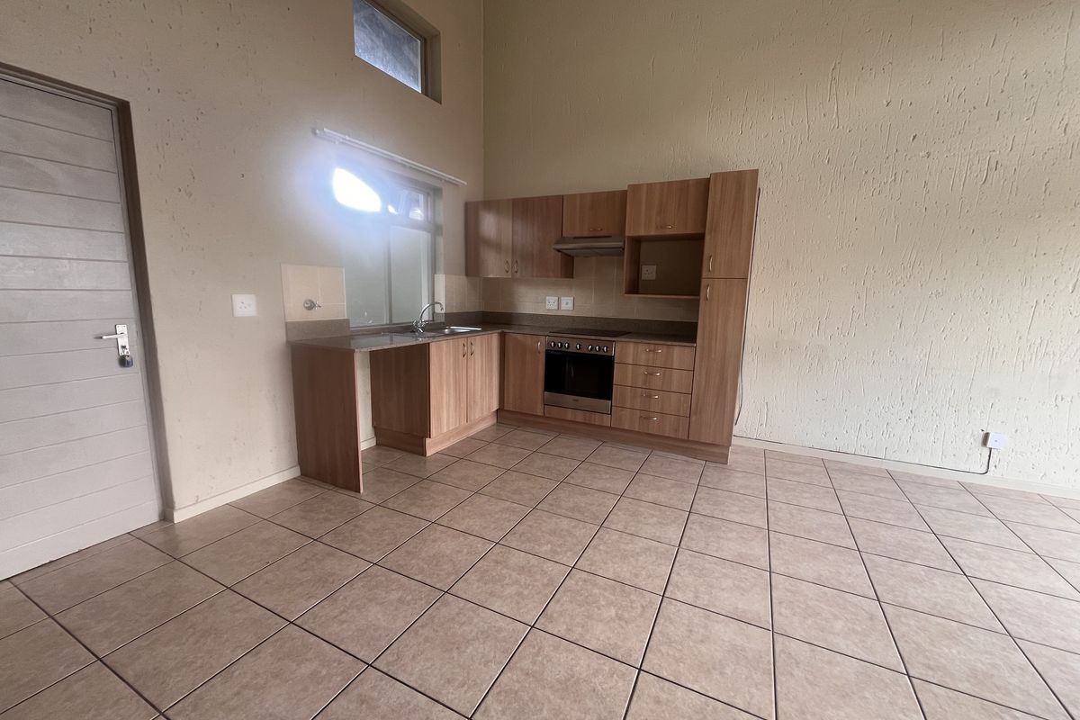 An empty kitchen featuring built-in wooden cabinetry, integrated oven and hob, ceramic floor tiles, and high ceilings with textured wall finishes.