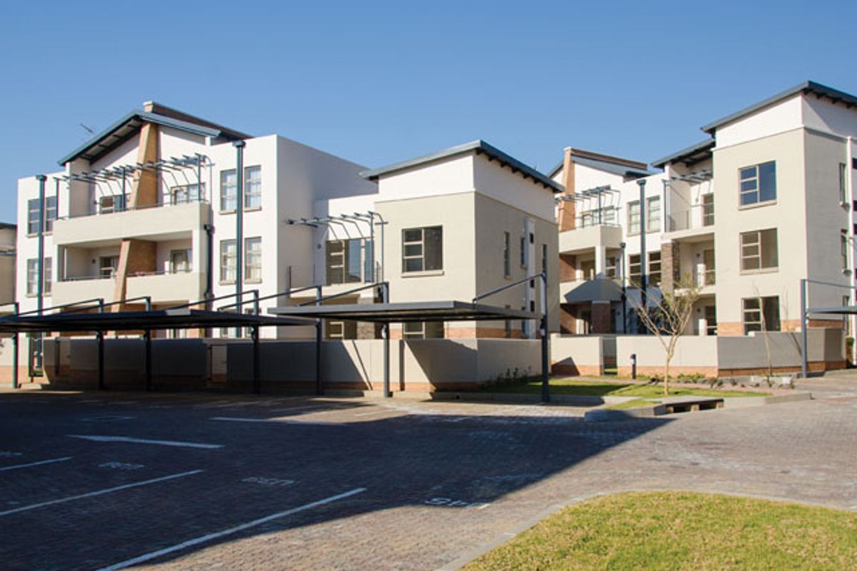 Exterior view of a modern multi-story apartment complex featuring paved parking areas, covered carports, and private balconies.