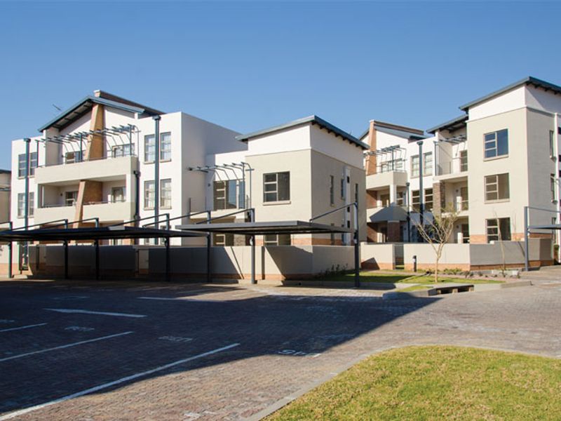 Exterior view of a modern multi-story apartment complex featuring paved parking areas, covered carports, and private balconies.