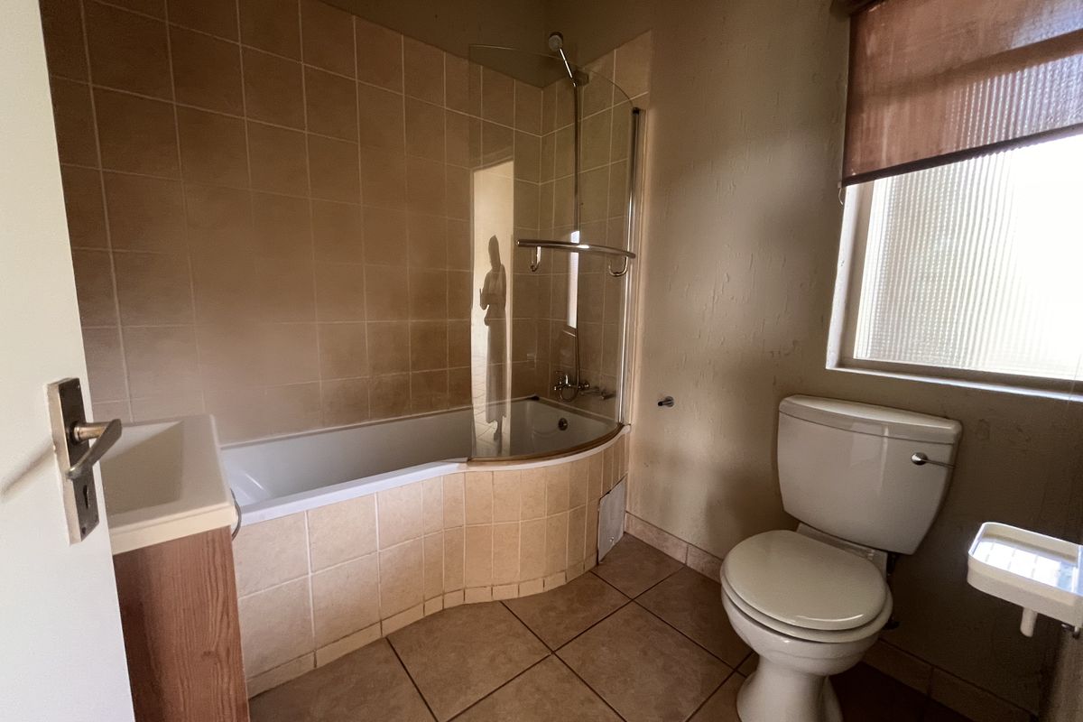 A dated bathroom featuring a built-in bathtub with a glass screen, a standard toilet, and a vanity cabinet with tiled finishes throughout.