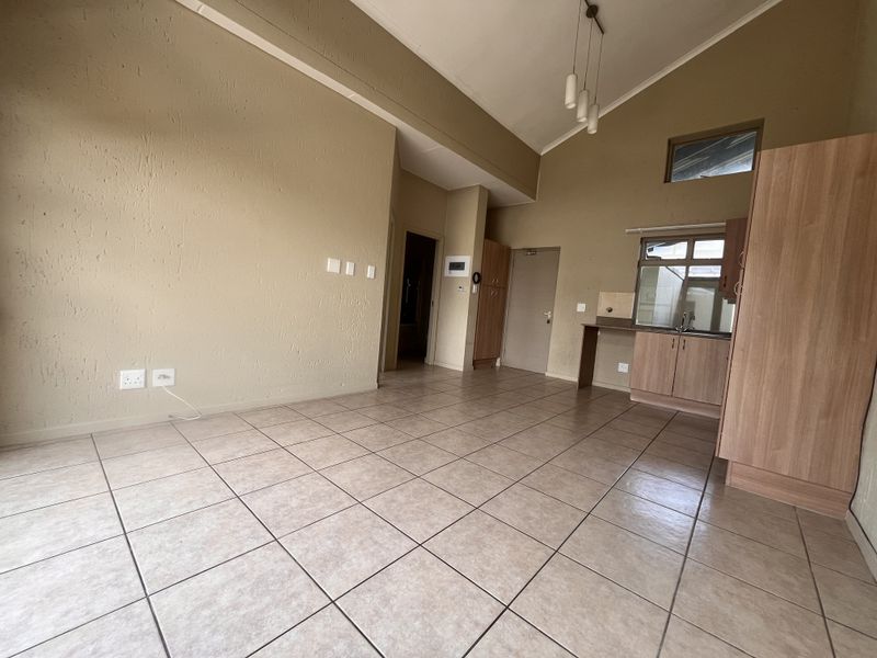 An open-plan living and kitchen area featuring tiled flooring, vaulted ceilings, and built-in cabinetry, offering a versatile space ready for personalization.