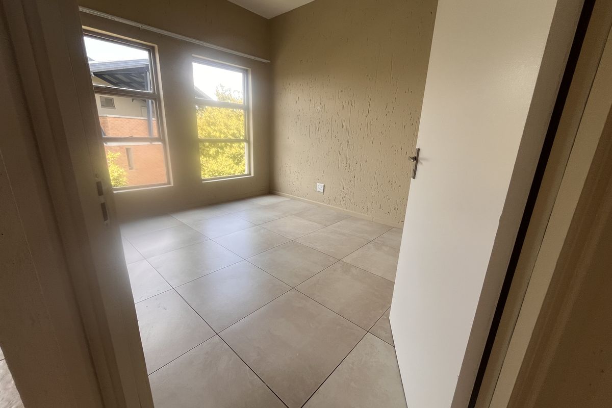 An empty bedroom featuring neutral tiled flooring, textured wall finishes, and large windows providing natural light.