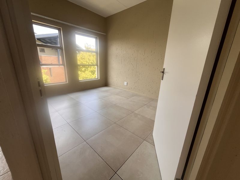 An empty bedroom featuring neutral tiled flooring, textured wall finishes, and large windows providing natural light.