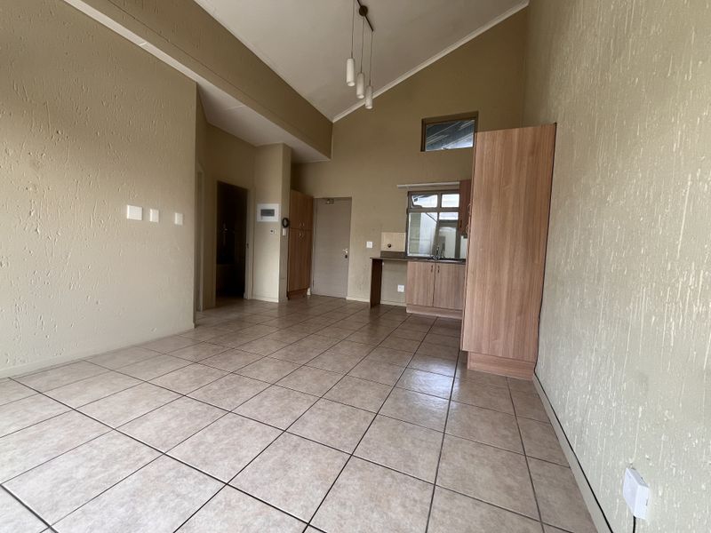 An open-plan living and kitchen area featuring vaulted ceilings, tiled flooring, and built-in cabinetry with a sink.