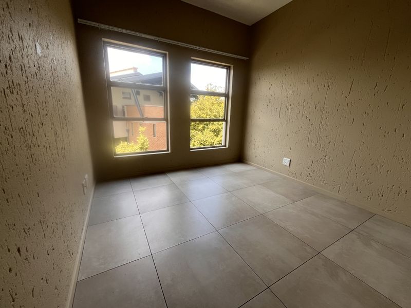 An empty bedroom featuring neutral tiled flooring, textured wall finishes, and large windows providing natural light.