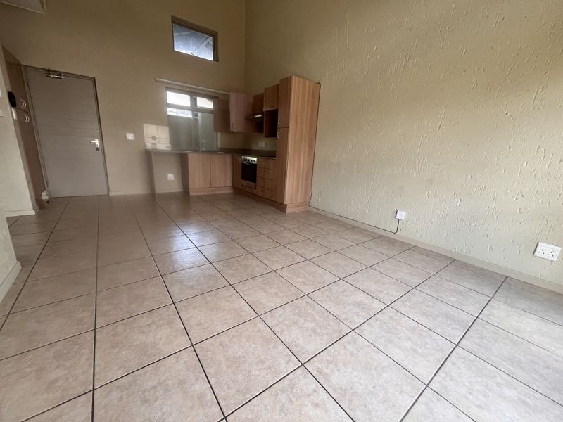 An open-plan living and kitchen area featuring tiled floors, high ceilings, and functional built-in cabinetry with an integrated oven and extractor fan.