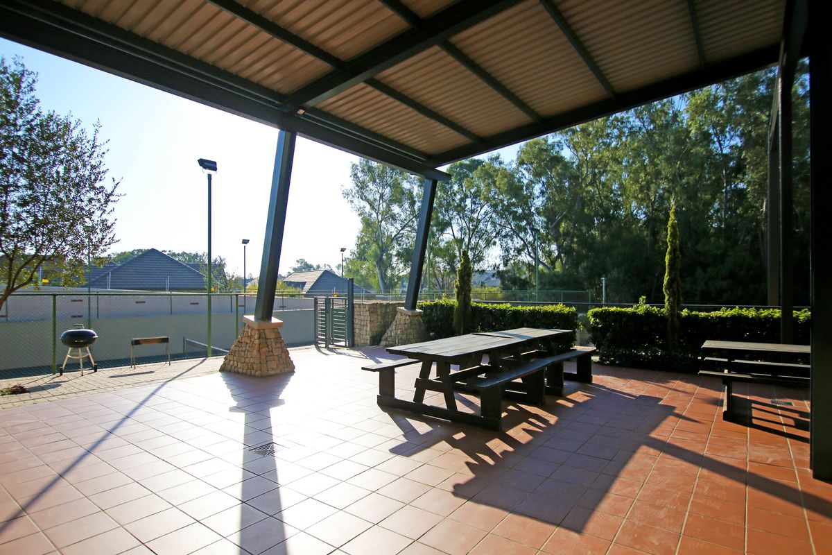 A spacious covered patio area featuring tiled flooring, stone-clad support pillars, and a metal roof, overlooking a fenced outdoor recreational space.