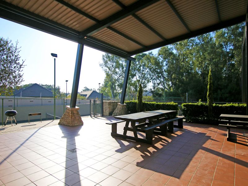 A spacious covered patio area featuring tiled flooring, stone-clad support pillars, and a metal roof, overlooking a fenced outdoor recreational space.