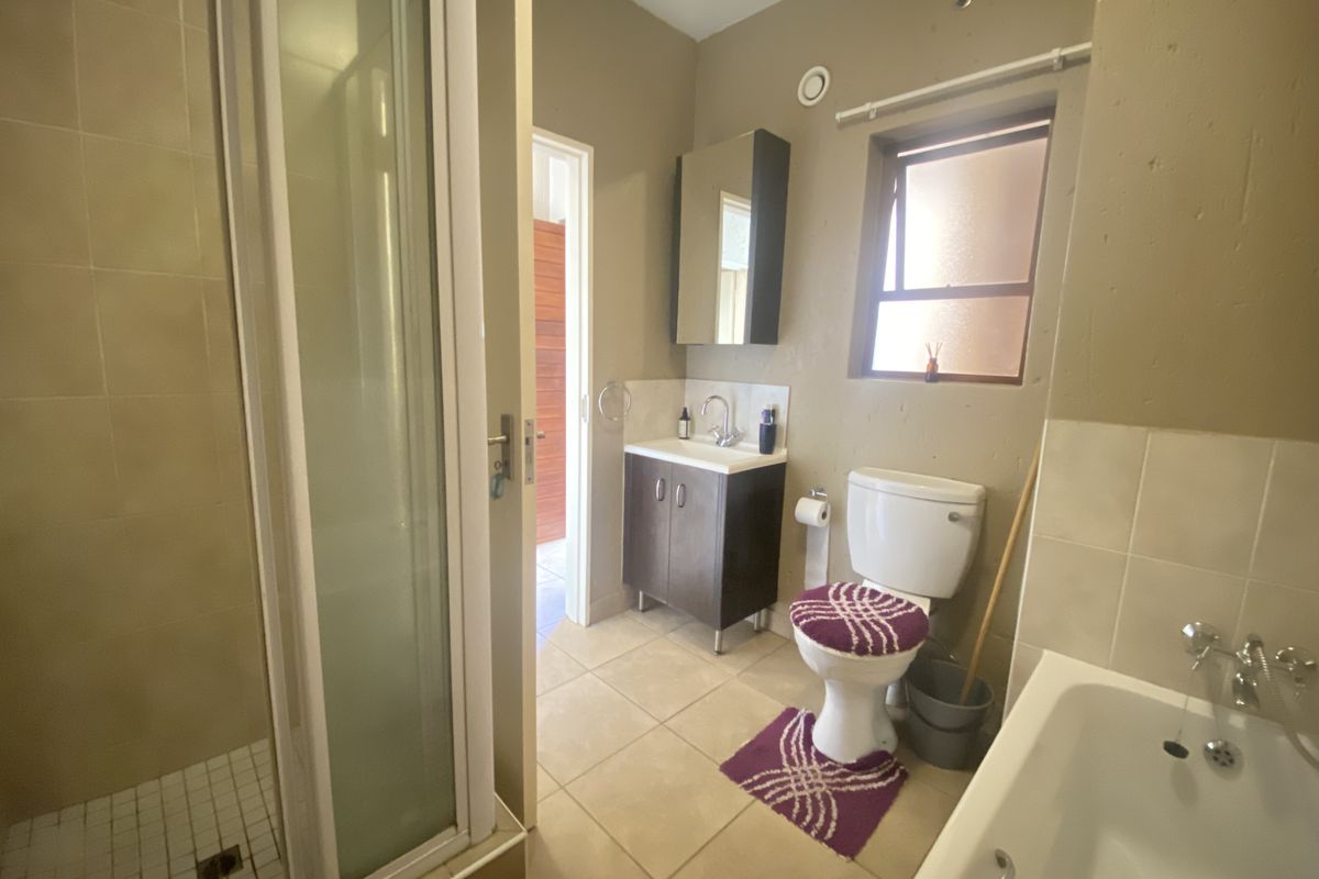 A functional bathroom featuring a shower enclosure, bathtub, vanity cabinet with basin, and toilet, finished with neutral wall tones and tiled flooring.