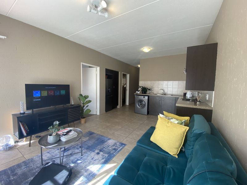 Open-plan living area featuring a compact kitchen with built-in cabinetry, tiled backsplash, and integrated laundry space, flowing into a comfortable lounge area.