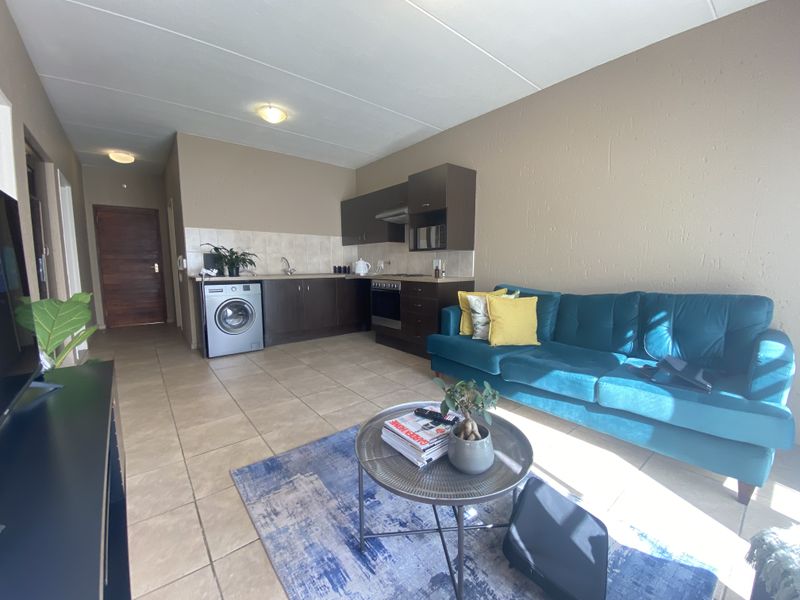 Open-plan living area featuring a compact kitchen with built-in cabinetry, tiled flooring, and integrated appliances, seamlessly flowing into the lounge space.