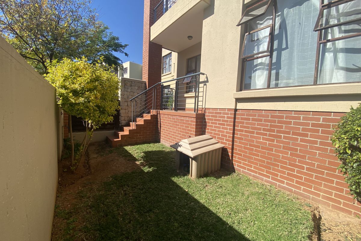 A rear exterior view of the apartment featuring a brick facade, a small private garden area, and a brick staircase leading to the entrance.