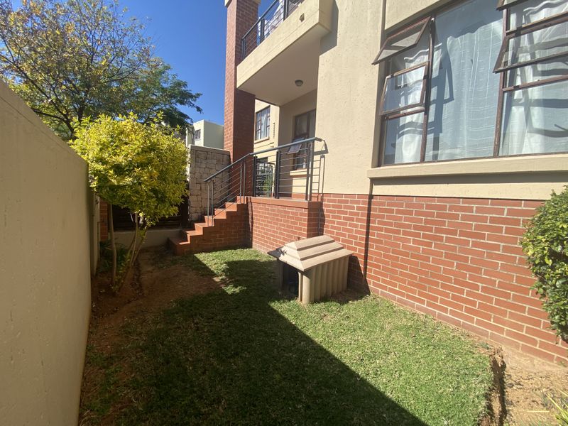 A rear exterior view of the apartment featuring a brick facade, a small private garden area, and a brick staircase leading to the entrance.