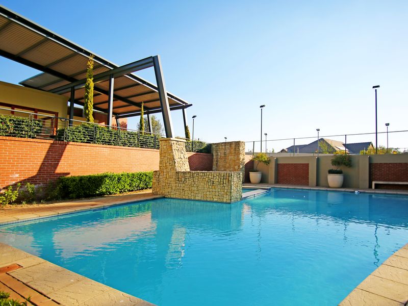 A well-maintained outdoor pool area featuring a stone water feature, brick boundary walls, and a covered patio structure for outdoor relaxation.