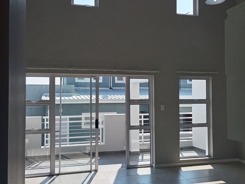 Spacious open-plan living area featuring high ceilings, large tiled floors, and sliding glass doors leading to an outdoor balcony.