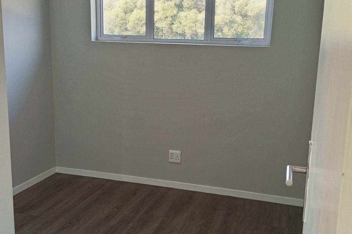 A clean, empty bedroom featuring modern laminate flooring, neutral grey walls, and a horizontal window providing natural light.