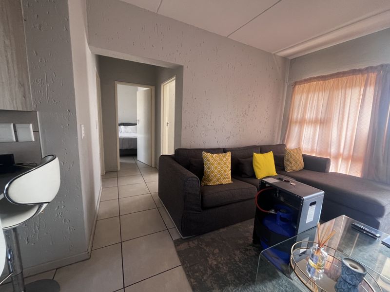 A living room area featuring tiled flooring, textured wall finishes, and a coved ceiling, providing access to adjacent rooms.