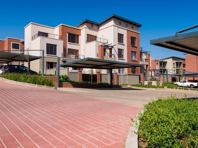 Exterior view of a modern apartment complex featuring brick and plaster facades, private balconies, and covered parking bays.