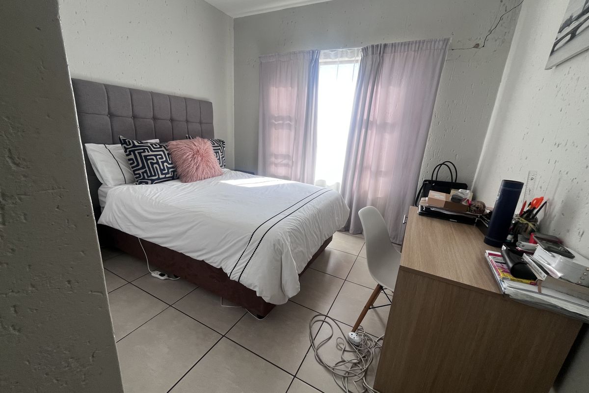 A compact bedroom featuring tiled flooring and natural light, currently showing visible wall plaster cracking that requires maintenance.