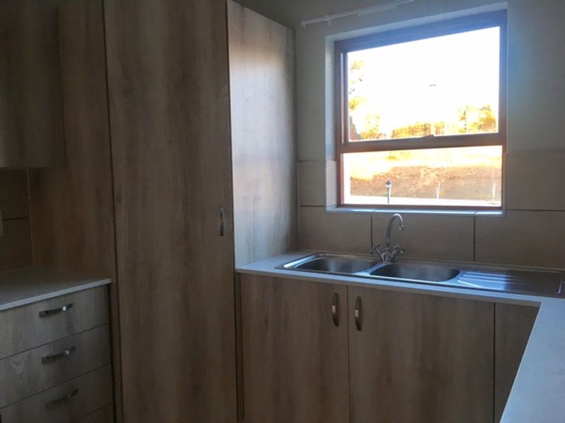 A clean, modern kitchen featuring light wood-grain cabinetry, a double bowl stainless steel sink with a mixer tap, and neutral tiled splashbacks.