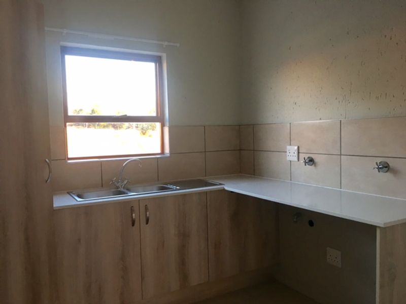 A clean, functional laundry area featuring light wood-finish cabinetry, a double sink, and tiled splashbacks with dedicated plumbing and electrical points.