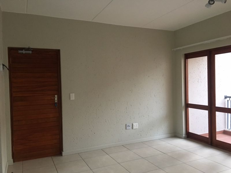 An empty living room featuring neutral textured walls, tiled flooring, a wooden door, and a sliding glass door providing access to an outdoor area.