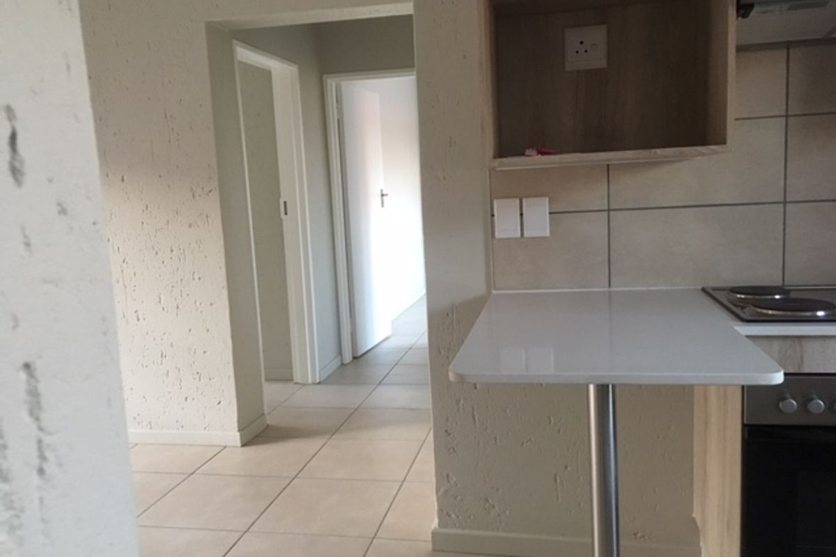 A functional kitchen area featuring a breakfast bar, built-in oven, electric hob, and tiled flooring, leading into a hallway.