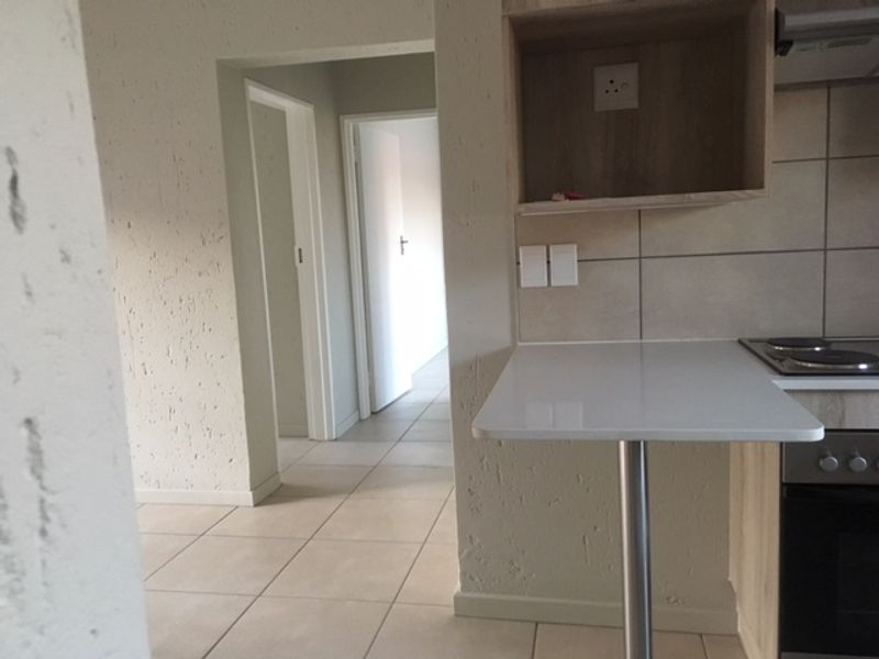 A functional kitchen area featuring a breakfast bar, built-in oven, electric hob, and tiled flooring, leading into a hallway.