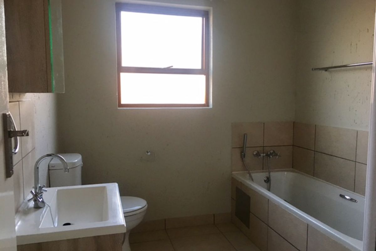 A functional bathroom featuring a vanity basin, toilet, and a bathtub with shower mixer, requiring minor cosmetic updates to the wall finishes.