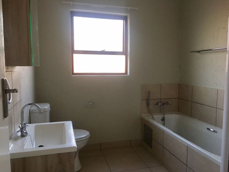 A functional bathroom featuring a vanity basin, toilet, and a bathtub with shower mixer, requiring minor cosmetic updates to the wall finishes.