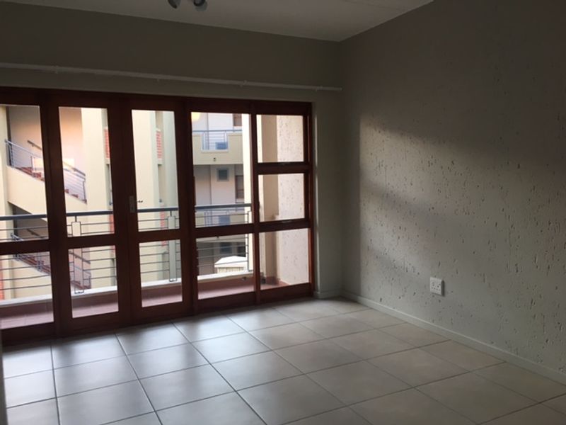 An empty living room featuring neutral tiled flooring, textured walls, and large timber-framed glass doors providing access to an external balcony area.
