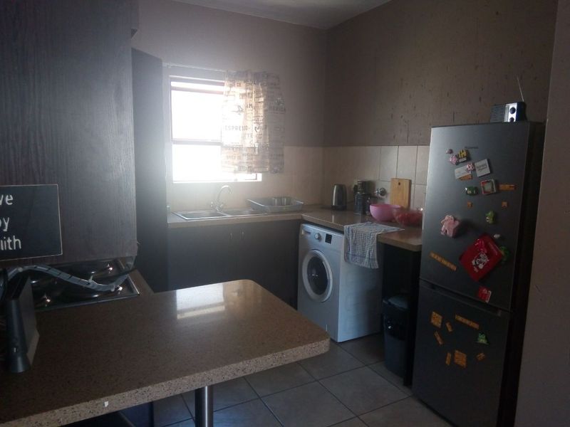 A functional kitchen featuring laminate countertops, built-in cabinetry, tiled flooring, and a stainless steel sink, with a dedicated space for laundry appliances.