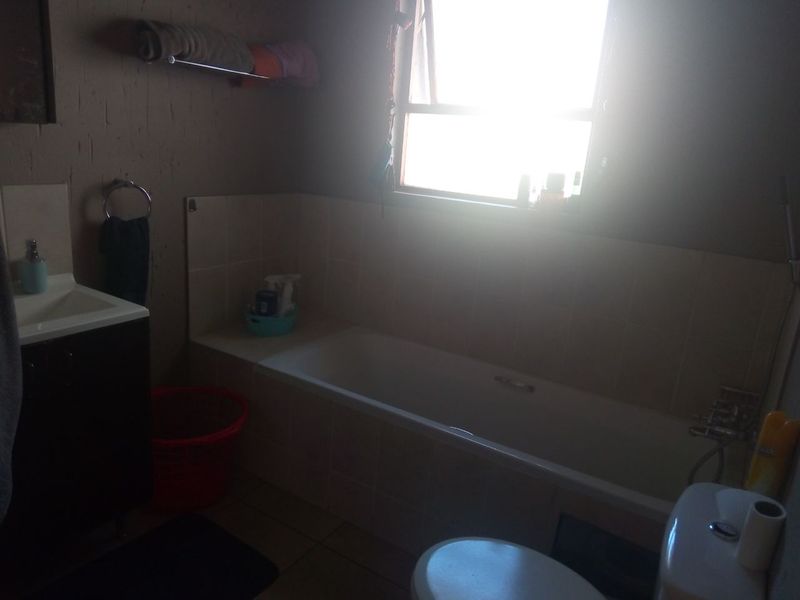 A functional bathroom featuring a built-in bathtub, vanity cabinet with basin, and toilet, with tiled splashback areas.