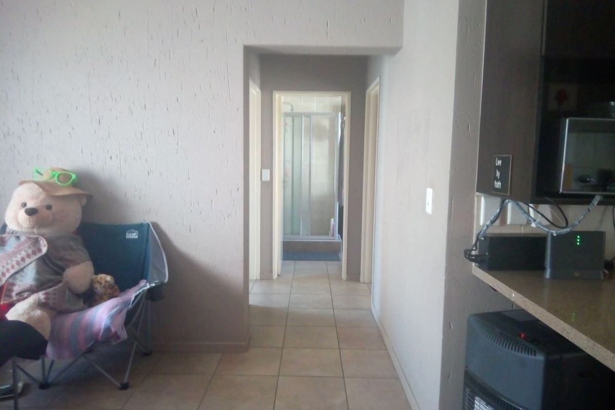 A hallway with tiled flooring and textured walls, providing access to other rooms including a bathroom visible at the end of the corridor.