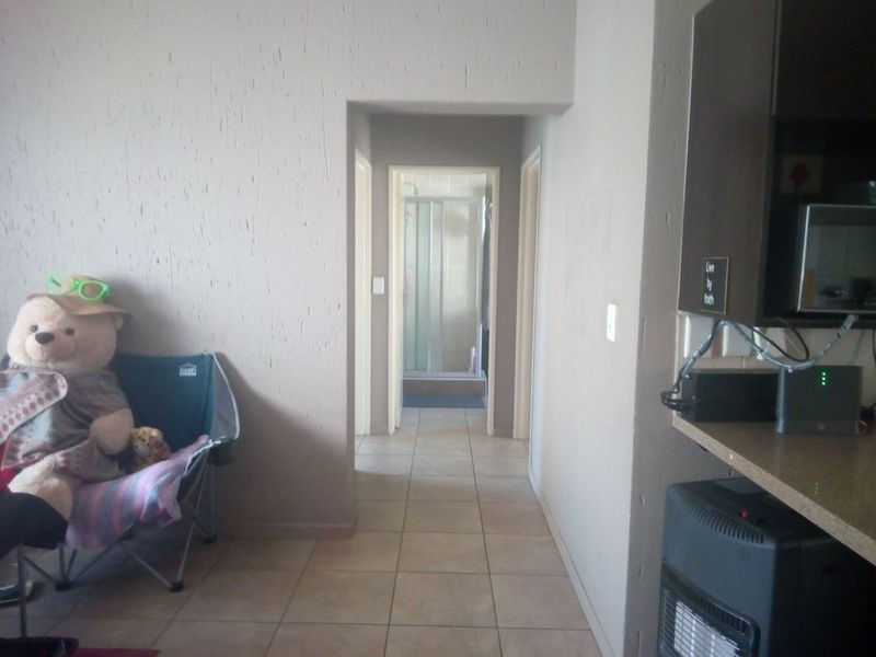A hallway with tiled flooring and textured walls, providing access to other rooms including a bathroom visible at the end of the corridor.