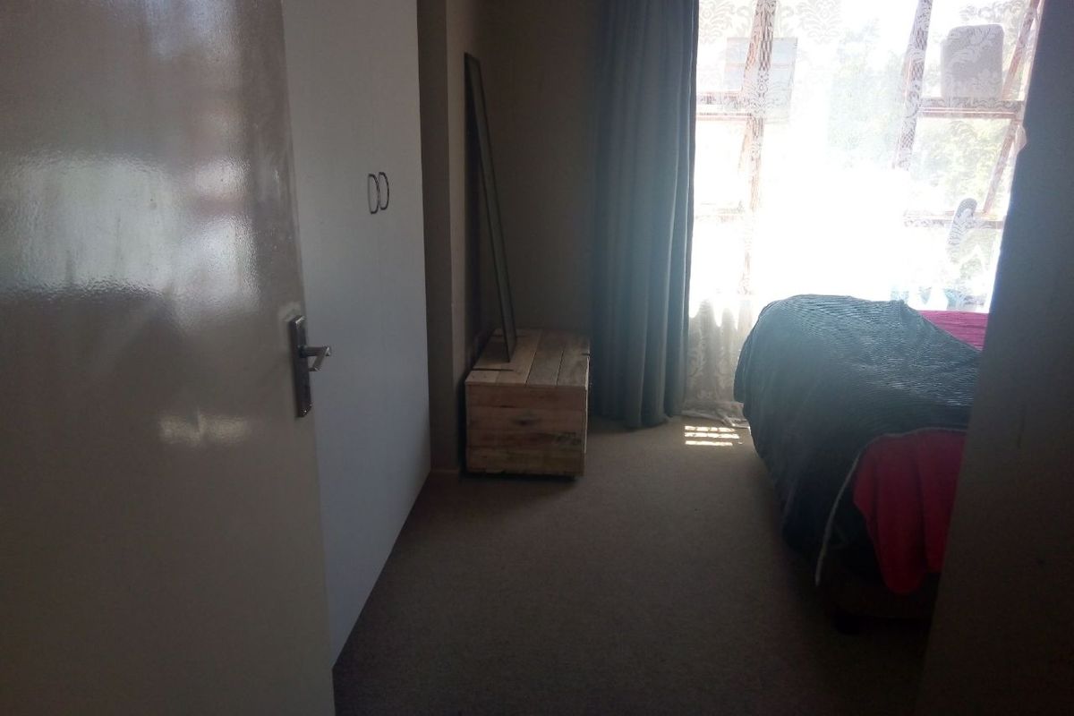 A bedroom featuring built-in cupboards and carpeted flooring, illuminated by natural light from a large window.