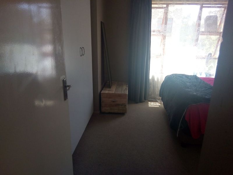 A bedroom featuring built-in cupboards and carpeted flooring, illuminated by natural light from a large window.
